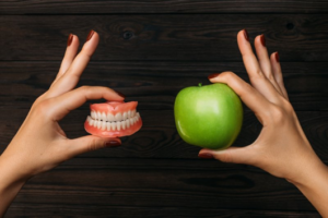 Left hand holding dentures and right hand holding an apple